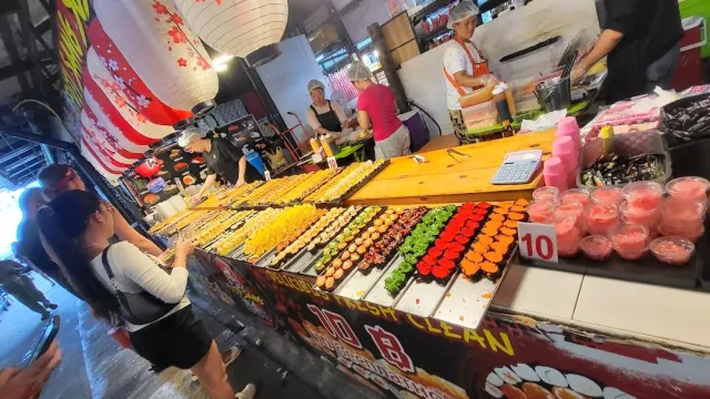 A sushi stall with colorful rows on a wooden counter, a paper lantern hanging above