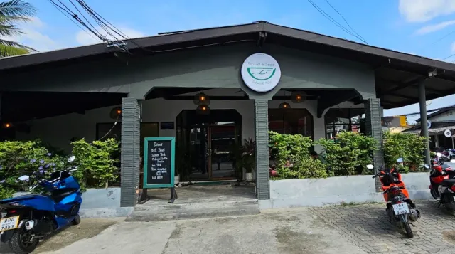 A gray building with a round sign, a menu board and motorbikes parked out front