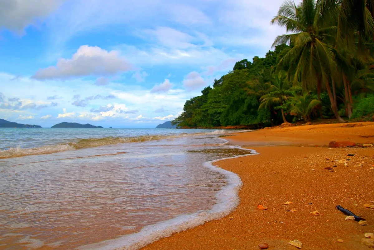 Curving golden sand beach with gentle surf, leaning palms and islands on the horizon