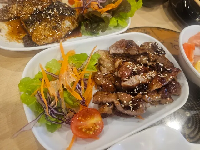 Grilled pieces of meat with sesame beside a vegetable salad and tomato