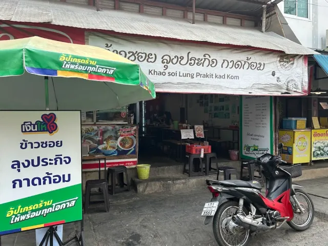 A simple stall front with a cloth sign, a green umbrella and a motorbike parked in front