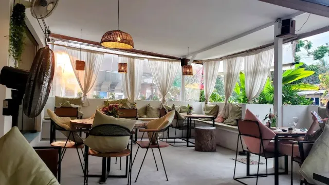 A covered dining space with white curtains, rattan lamps and a bench padded with cushions