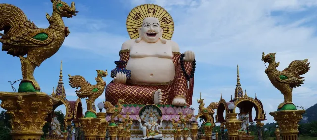 A giant white laughing Buddha figure on a base decorated in gold and pink