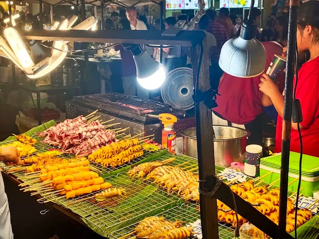 Skewers and seafood on a grill at a lit street stall in the evening