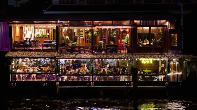 A lit two storey building on the waterfront at night, full of diners