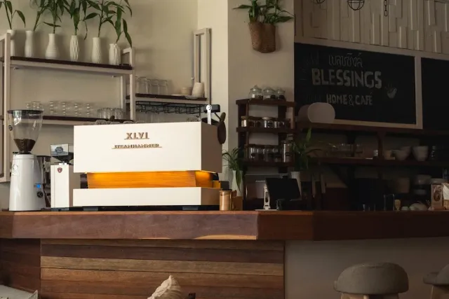 A wooden cafe counter with a white espresso machine and shelves of dishes behind