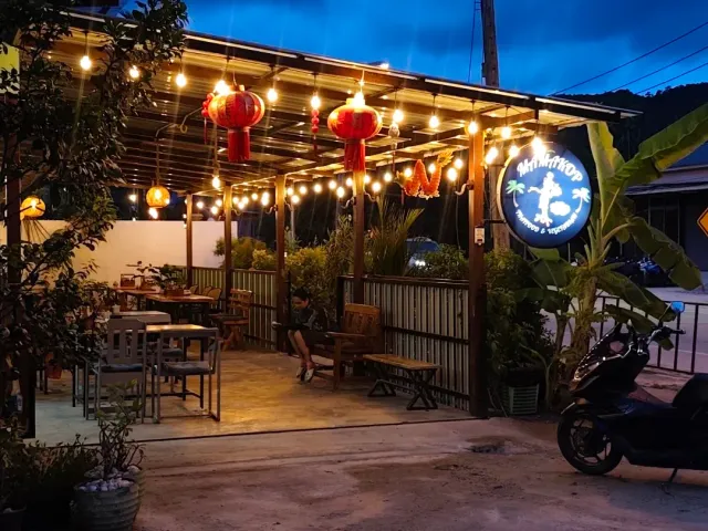A pergola lit at night with red lanterns, high tables and a round sign to the side