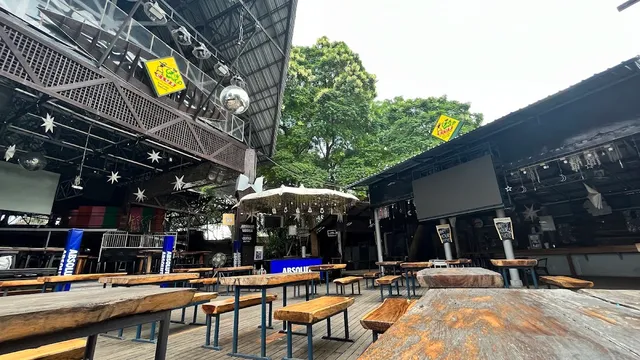 An open courtyard with wooden benches, a disco ball and large screens by day