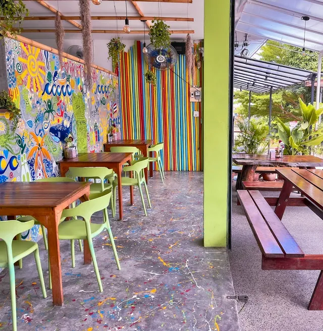 A seating area with colorful murals, wooden tables and green chairs
