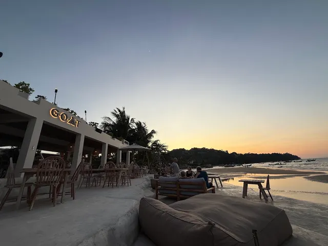A terrace with wooden chairs and beanbags on the beach at sunset during low tide