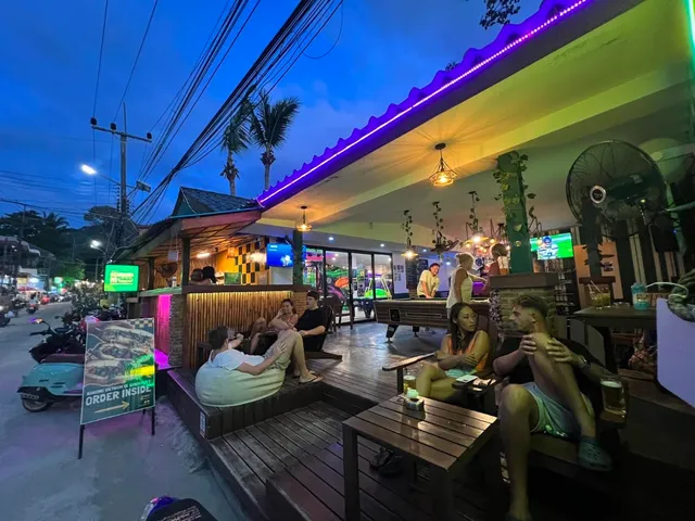 A wooden deck with guests, a pool table and purple lighting in the evening