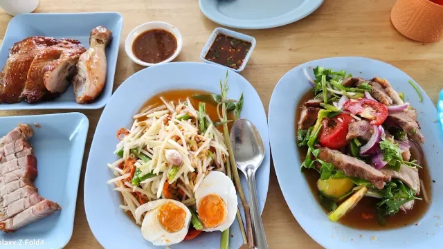 A tray of plates with pink meat slices, papaya salad with eggs and a spicy salad