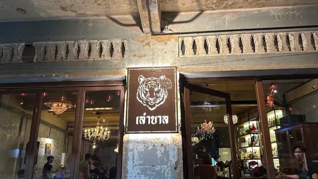 A peeling concrete facade with a tiger head sign, open wooden doors and chandeliers inside