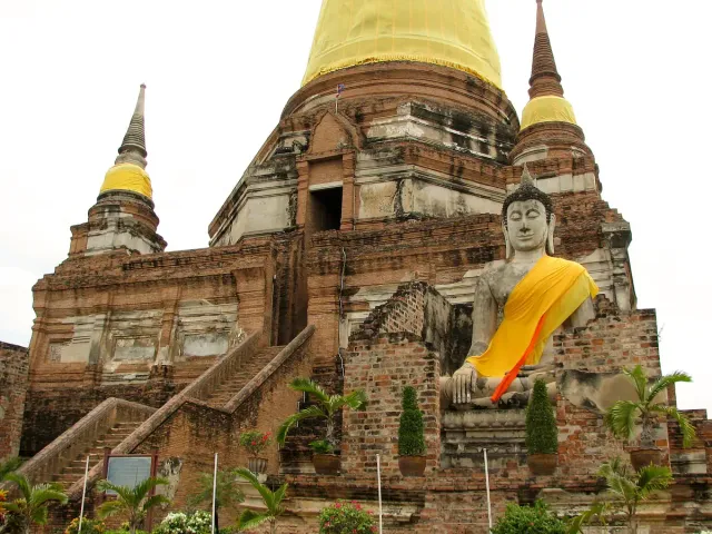 A tall brick chedi with a Buddha figure draped in an orange robe at its front