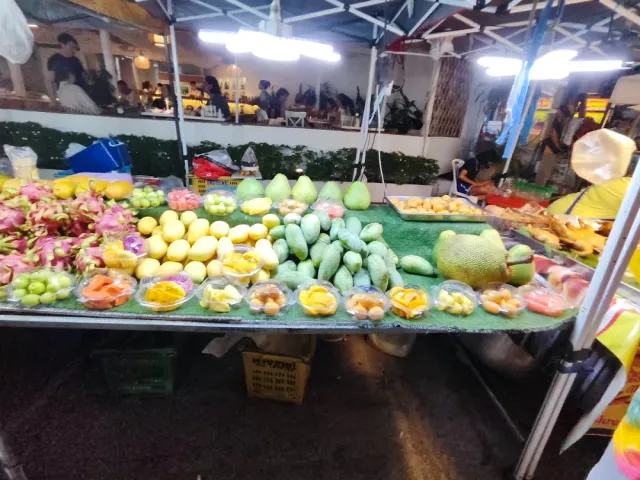 A lit tropical fruit stall, mango, dragon fruit and jackfruit laid out on the table