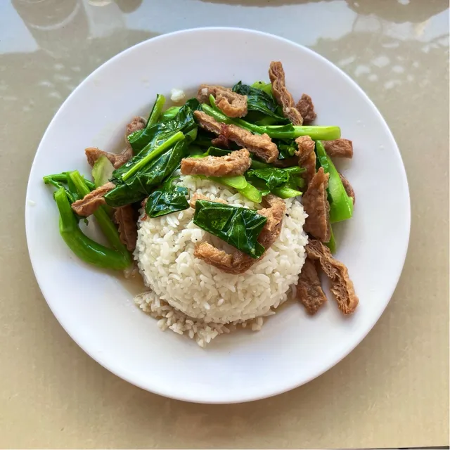A plate of white rice with stir-fried greens and crispy brown strips