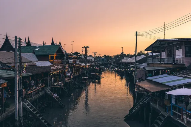 A water canal between traditional wooden houses at sunset, with boats moored along the bank