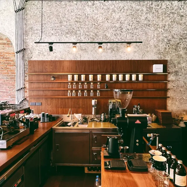A preparation counter with wooden shelves, jars, a grinder and an espresso machine against a concrete wall