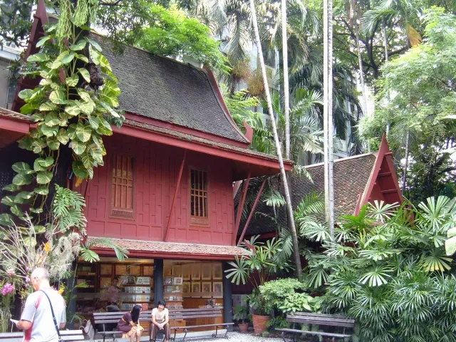 A two storey red teak house set inside a dense tropical garden