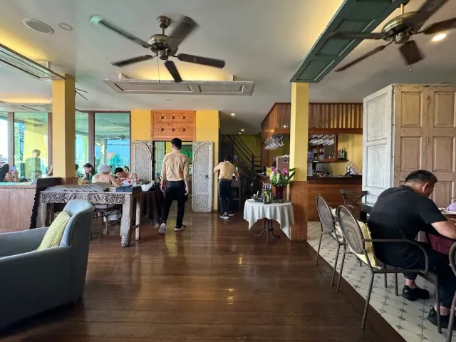 A dining room with a wooden floor, yellow columns, ceiling fans and diners by the windows