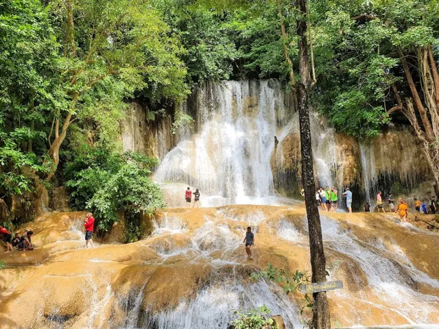 A waterfall spreading over brown rock steps with visitors standing in the water