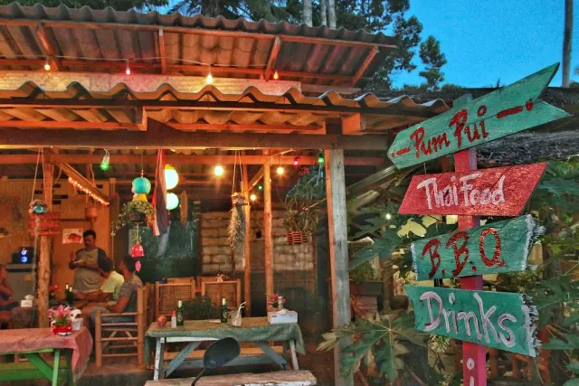 A wooden pavilion at dusk with hand painted arrow signs and colored bulbs