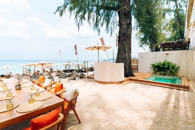A set table on the sand beside a small pool, with parasols and beanbags facing the sea