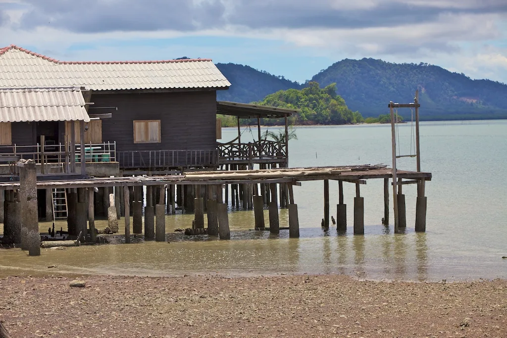 Wooden stilt houses over the water with an old jetty and green hills behind