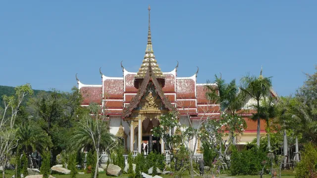 A white and gold temple hall with tiered roofs and a pointed spire under a blue sky