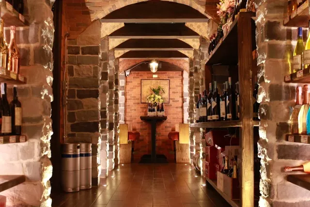 A stone cellar corridor with wine bottle shelves on both sides and warm lighting