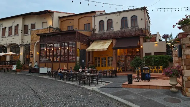 A paved square with European style buildings, string lights and outdoor tables