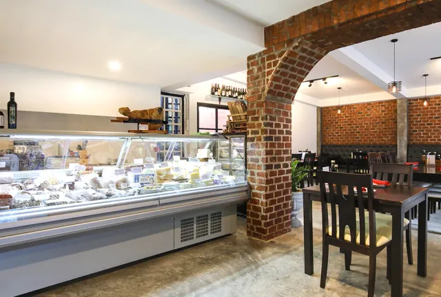A lit deli display with cheeses and cured meats, a brick arch and dining tables behind