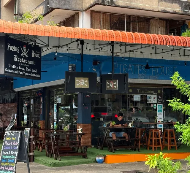 A blue front with signs and skull flags, outdoor tables and a menu board at the entrance