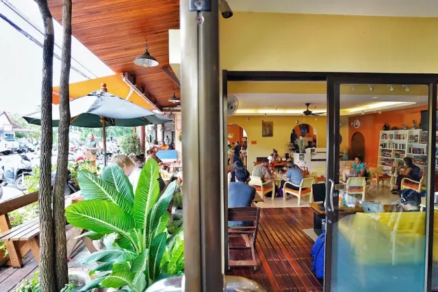A view inside a yellow space with diners and a bookshelf, and a terrace with a parasol