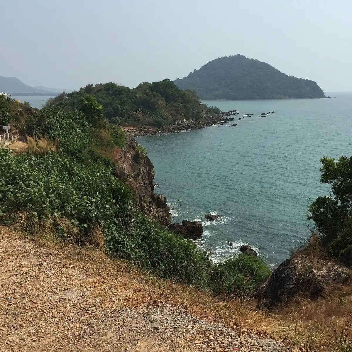 Scrub covered cliff dropping to a green bay with a forested headland beyond