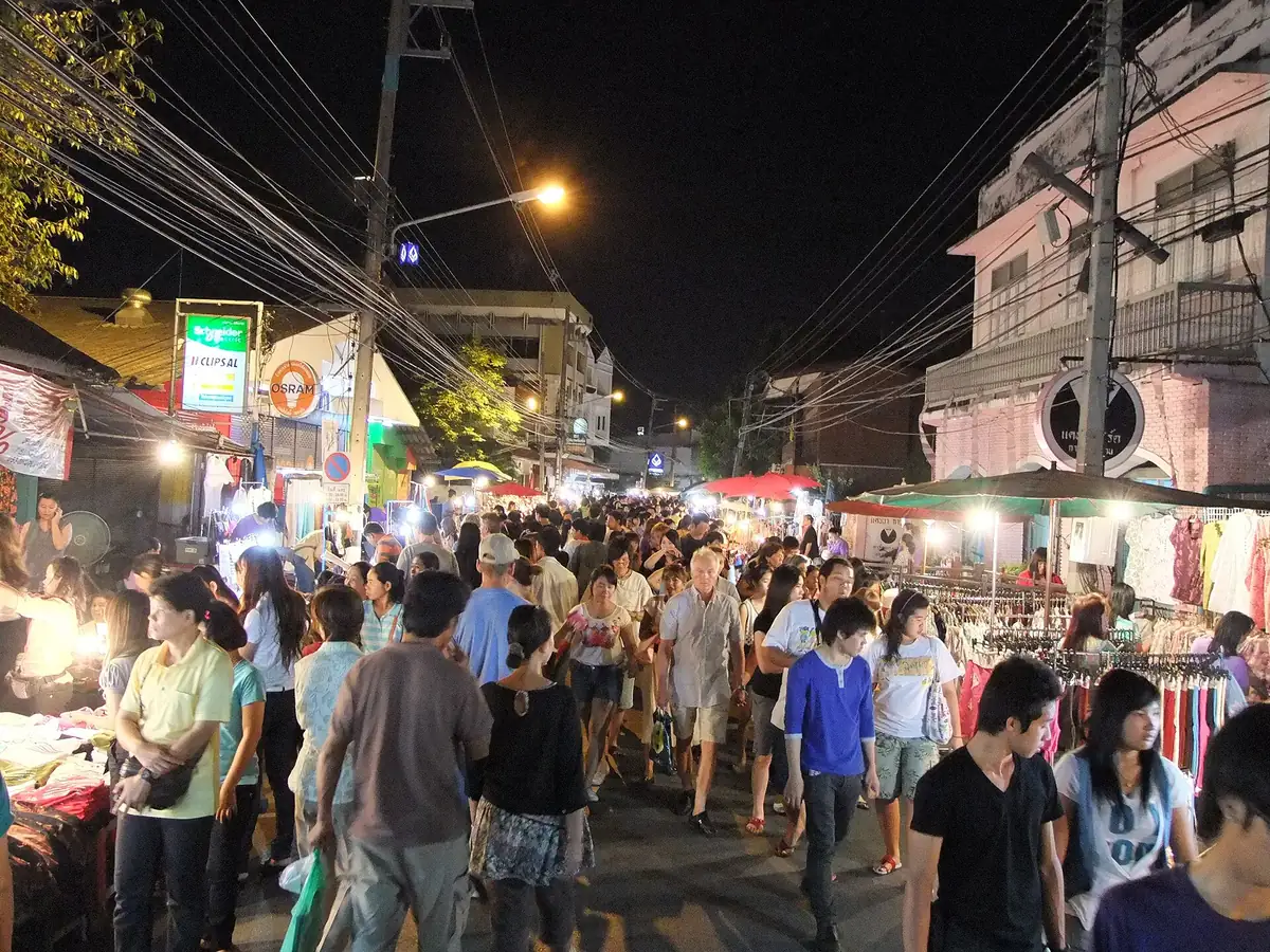 A street packed with an evening crowd, lit stalls and clothes hanging on both sides