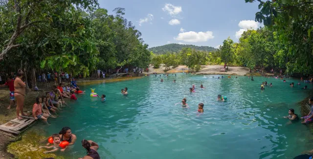 A natural pool of clear green water surrounded by forest, with bathers in it
