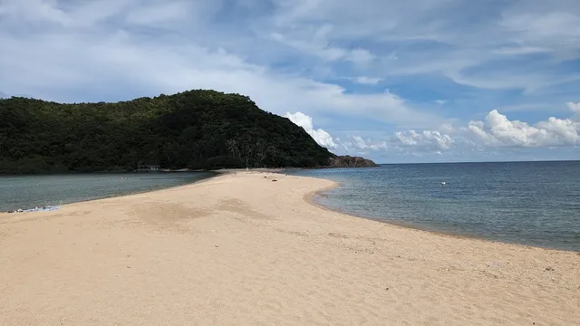 A strip of golden sand crossing the sea toward a jungle covered hill