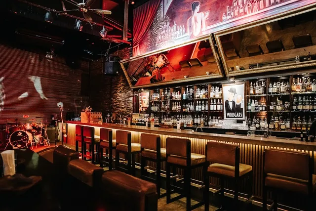 A long counter with leather bar stools, lit whisky shelves and a drum corner to the side