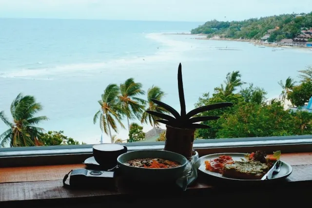 Breakfast on a window ledge facing a bay, palms and a camera beside the plates
