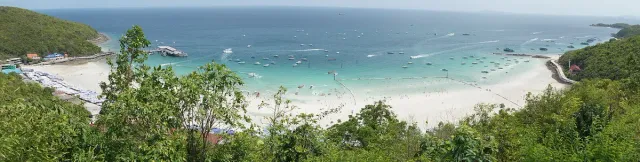 A panorama of a white sand bay with many boats and turquoise water