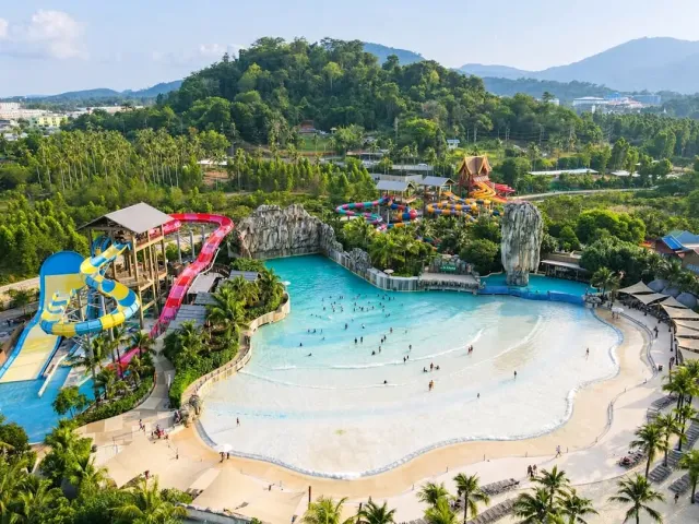 An aerial view of a large wave pool, colorful slides and forested hills