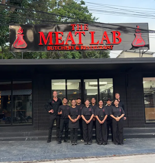 A staff in black clothing stands in front of a black facade with a red sign