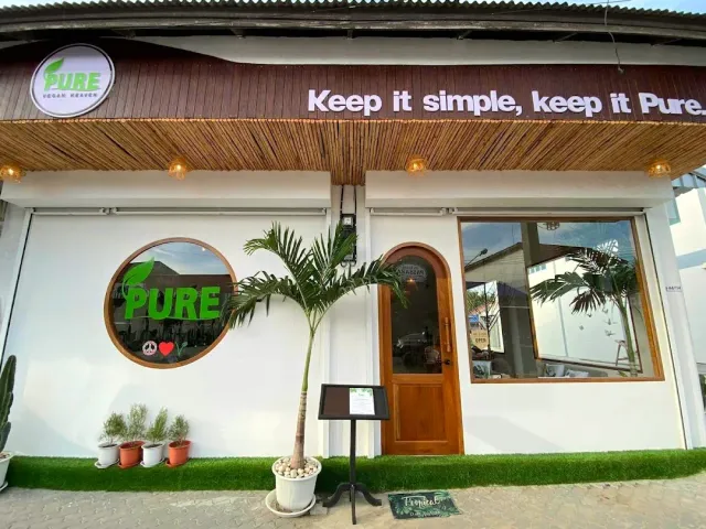 A white facade with a bamboo eave, green signs and a potted palm at the entrance