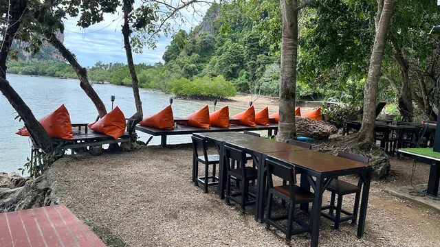 Orange cushions on benches along the water under trees and limestone cliffs