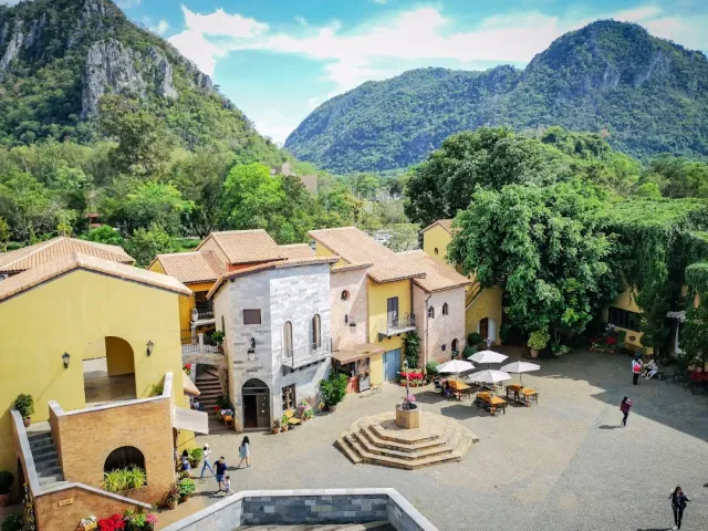 A paved plaza surrounded by yellow Italian style buildings facing green mountains