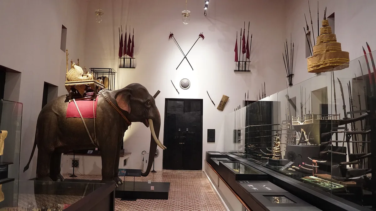 An exhibition hall with a harnessed war elephant model, weapons on the walls and glass display cases