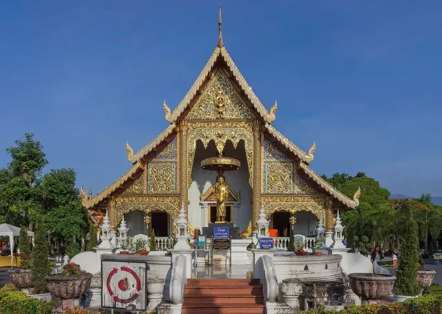 A Lanna style temple hall with dark tiered roofs and gilded decoration on its facade