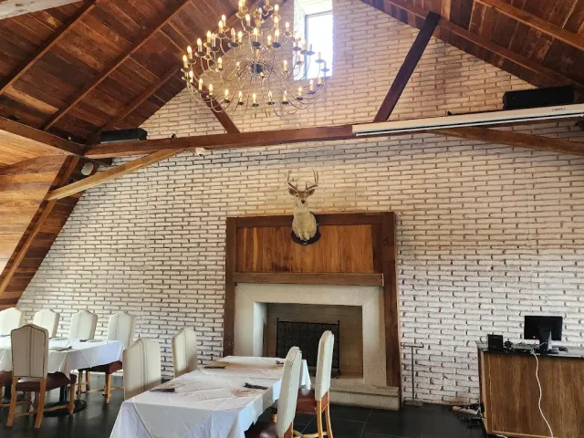 A white brick hall with a sloped wooden ceiling, a candle chandelier and set tables