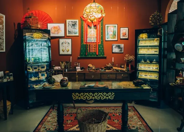 A space with orange walls, framed pictures, a dark wooden table and display cabinets